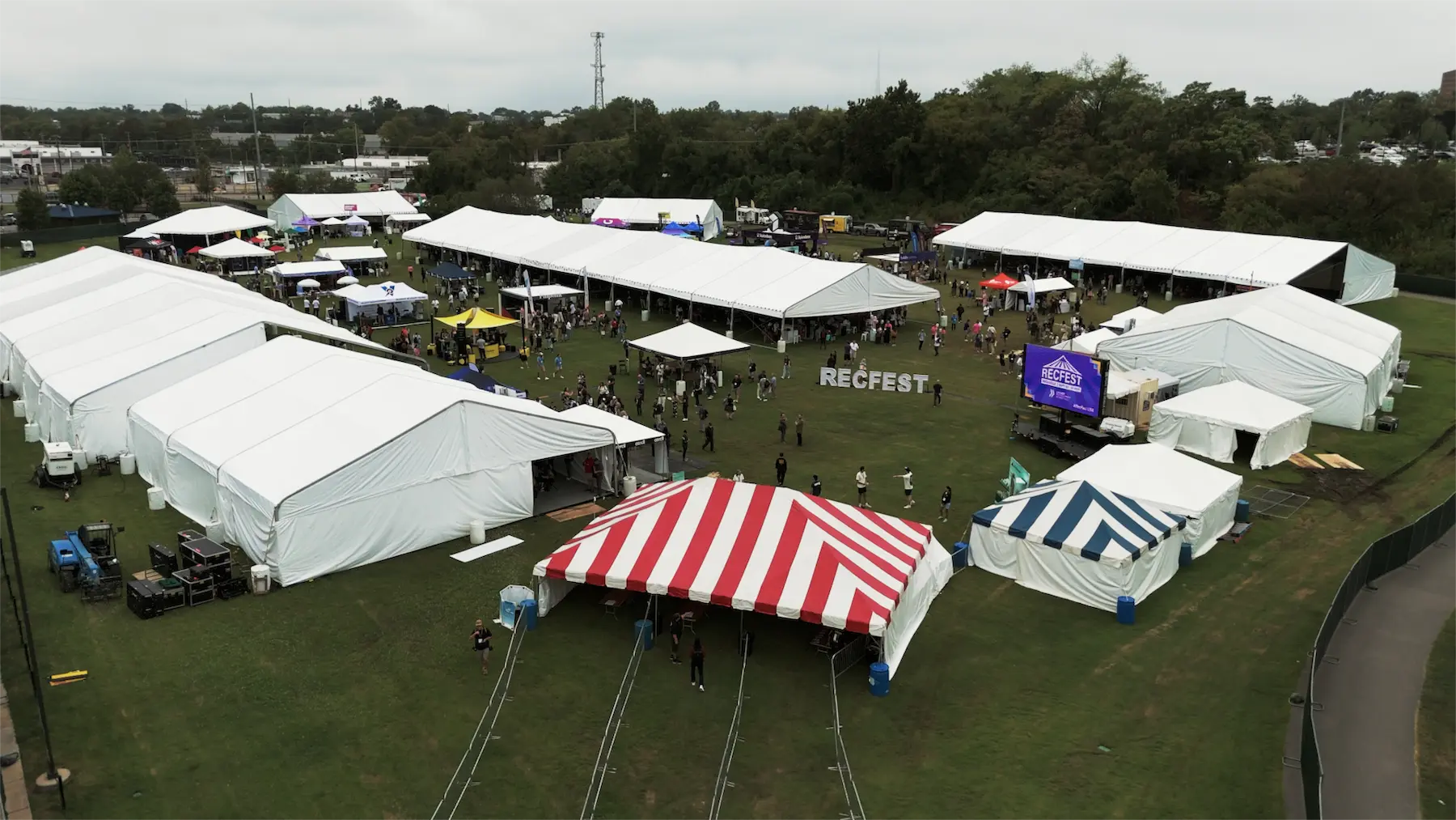 Arial shot of the Recfest event. A large field with a multi-coloured tent, and jundreds of people and stalls around a field lined with trees